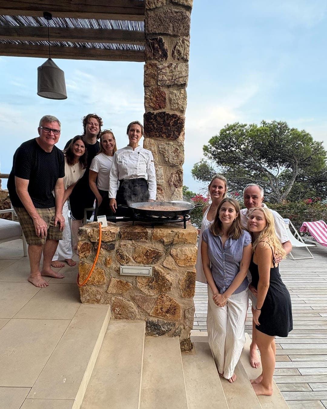 Chef Lara Petrella and guests around a paella pan on a villa terrace above the sea