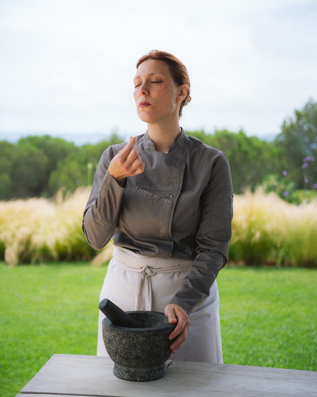 Chef Lara Petrella grinding fresh herbs with a mortar and pestle outdoors