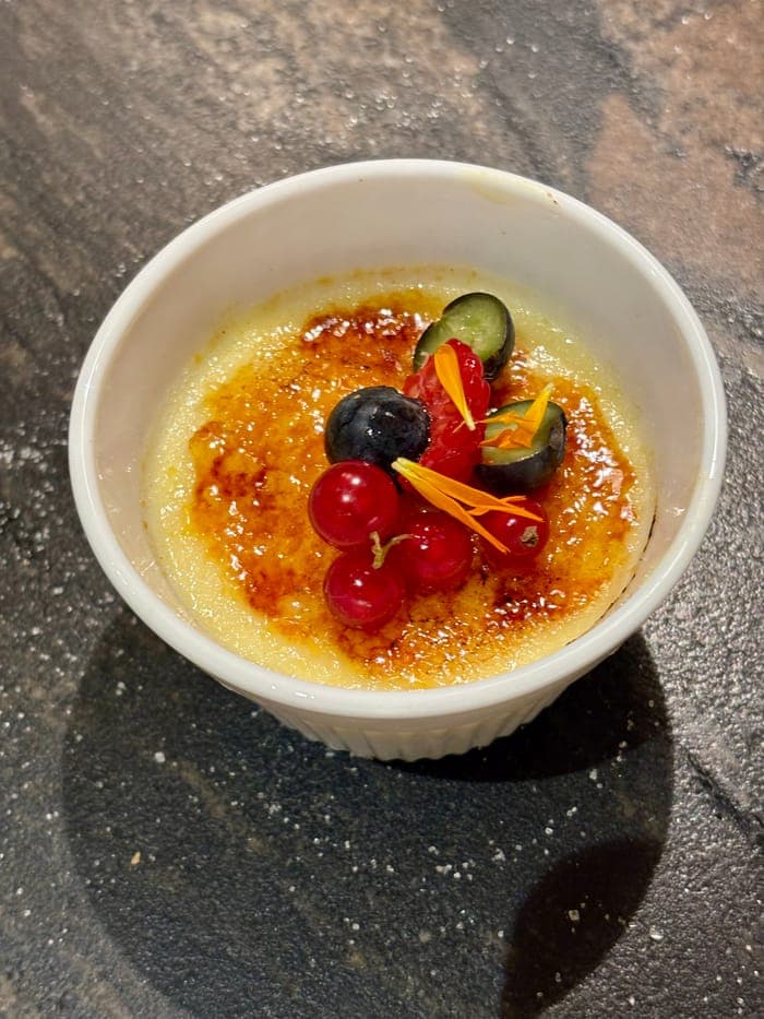 Crème brûlée topped with red currants, blueberries and edible flowers