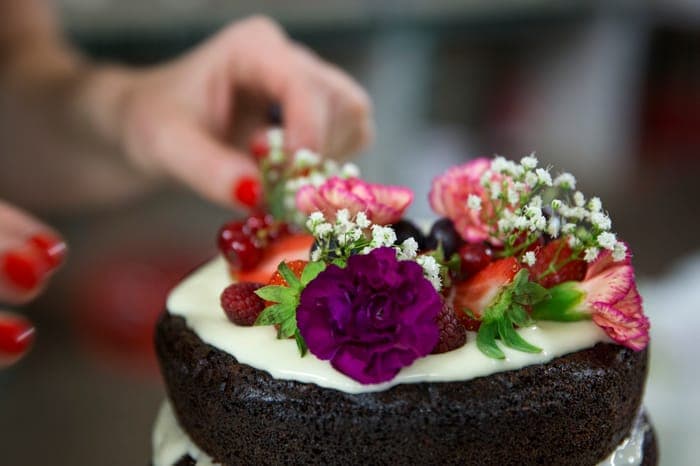 Chocolate cake being decorated with fresh berries and flowers